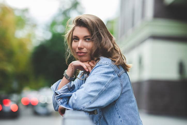 Hipster girl in clean white t-shirt and jeans posing against the background of buildings, minimalist urban clothing style