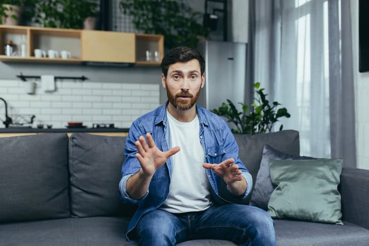 Concentrated man looking at webcam and talking on video call, sitting on sofa at home