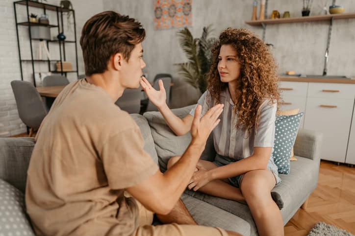 Young couple with relationship problems, sitting on the sofa in the living room and arguing.