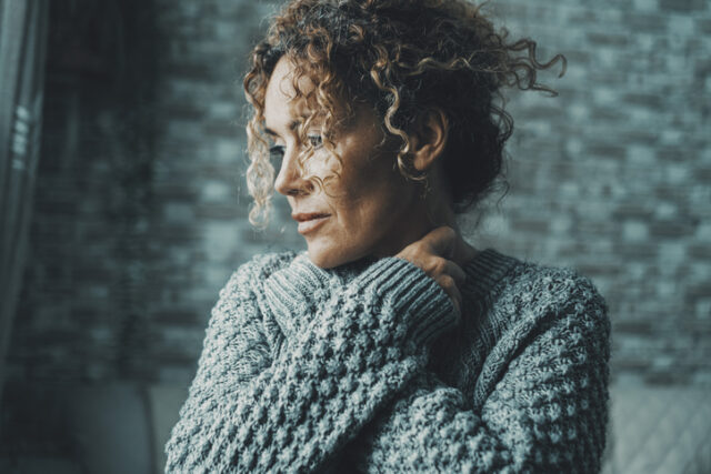Emotional feeling portrait of woman hugging herself with love and protection concept. Serene and intimate adult female people embracing her body and neck looking on her side outside the window