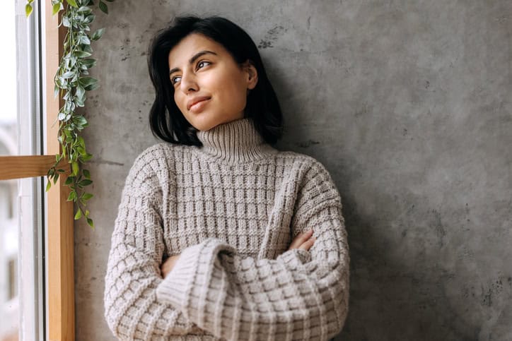 Portrait of young beautiful woman contemplating her thoughts while looking through window