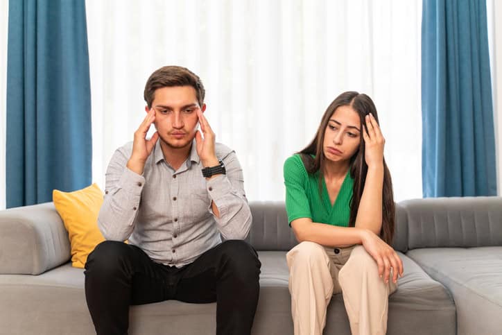 Young heterosexual couple arguing while sitting on sofa at home