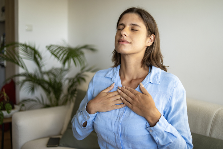 Woman sitting on sofa with closed eyes breathing.
