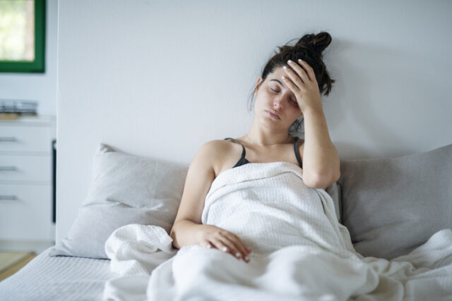 Sick young woman laying in bed under blanket.