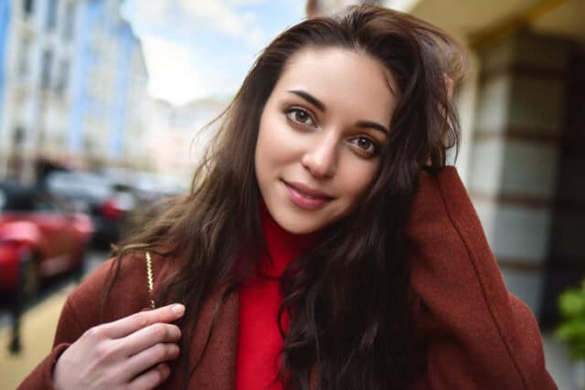 portrait of a fashionably dressed woman posing for the camera in a brown coat and red sweater