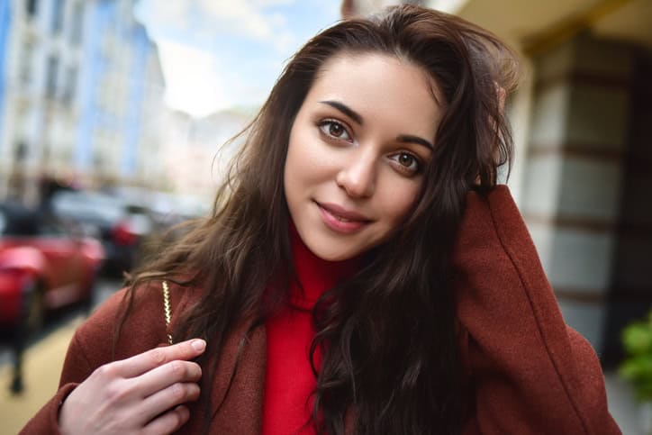 portrait of a fashionably dressed woman posing for the camera in a brown coat and red sweater