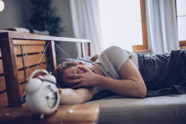 Sleeping man disturbed by alarm clock early in the morning.