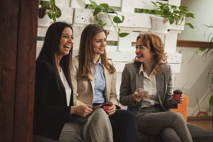 Three female colleagues are on a break from work, eating muffins and chatting.