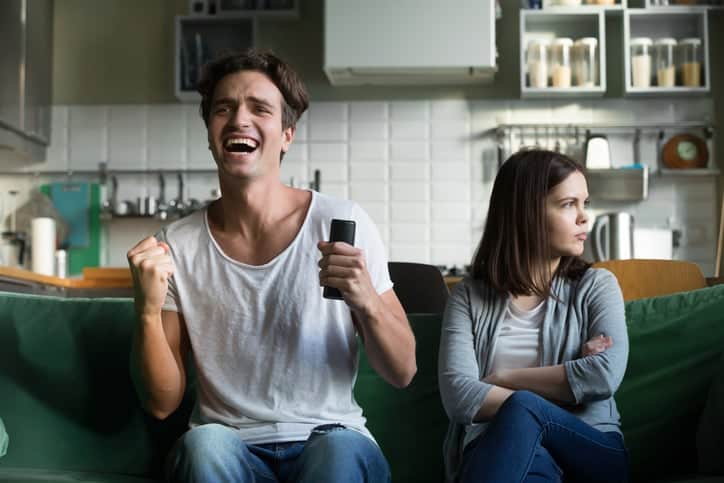 Angry girlfriend sulking while excited boyfriend watches sports.
