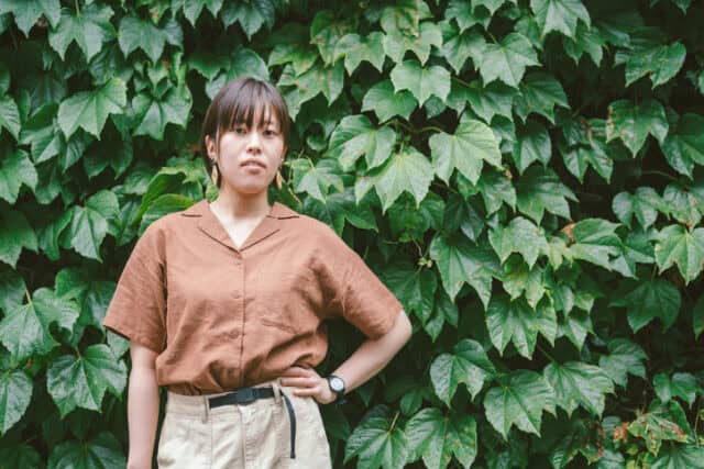 woman with hands in pocket in front of foliage