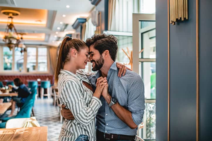 Young couple standing inside of cafeteria. The are huging and holding hands