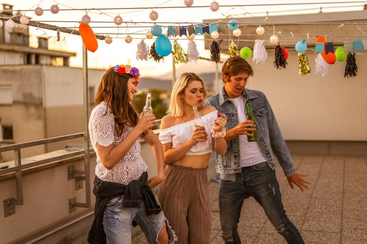 Young man and two young women having fun on a rooftop party at dusk.