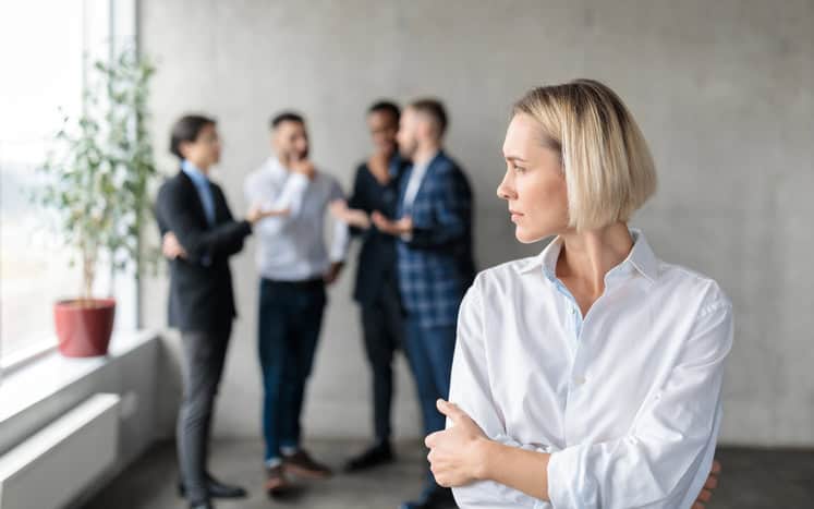 Woman standing alone as colleagues chat behind her.