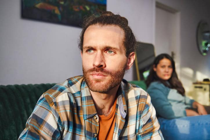 Cropped shot of a handsome young man looking annoyed after arguing with his girlfriend who is sitting in the background