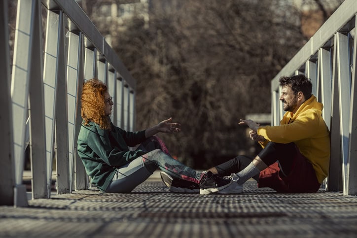 The girl explains to her friend what stretching exercises she wants to do while sitting on the footbridge and resting.