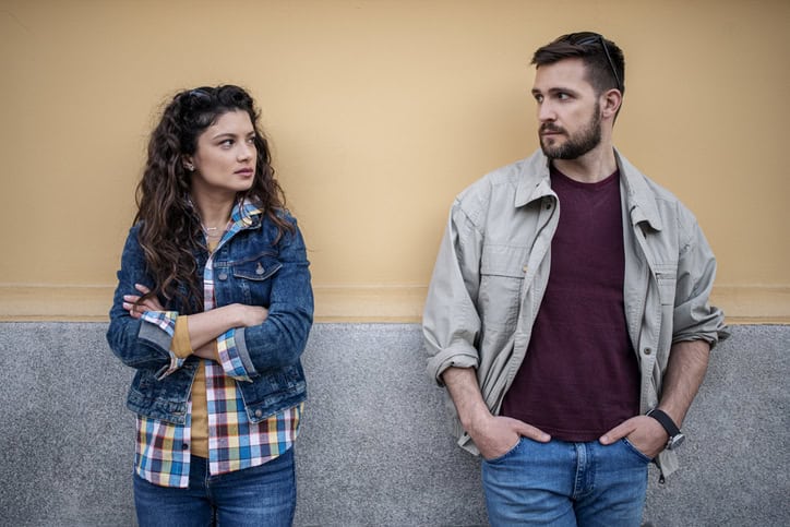 Friends standing beside a wall looking pensive.