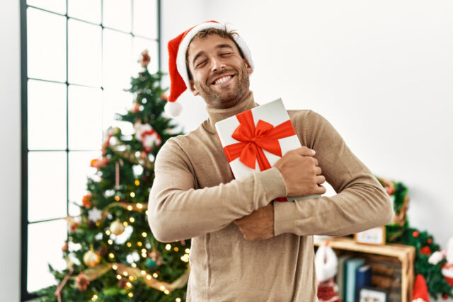 Man in Santa hat, holding a gift at home.