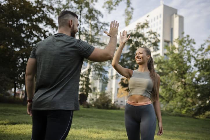 Two athletic people greeting each other with high five gesture during jogging workout