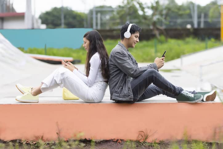 Young woman and young man sitting back to back using their cell phones