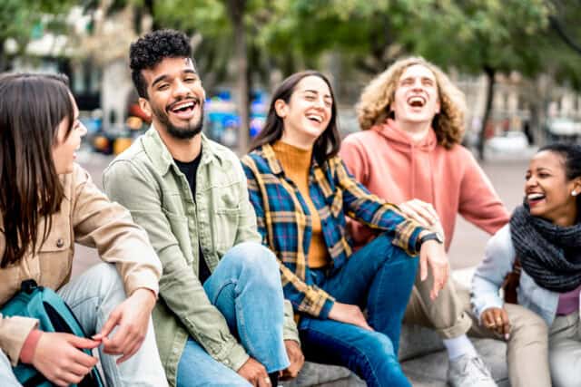 Millenial friends sitting together at city place on life style concept - Happy guys and girls having fun talking around Barceloneta streets - University students on travel vacation - Bright filter