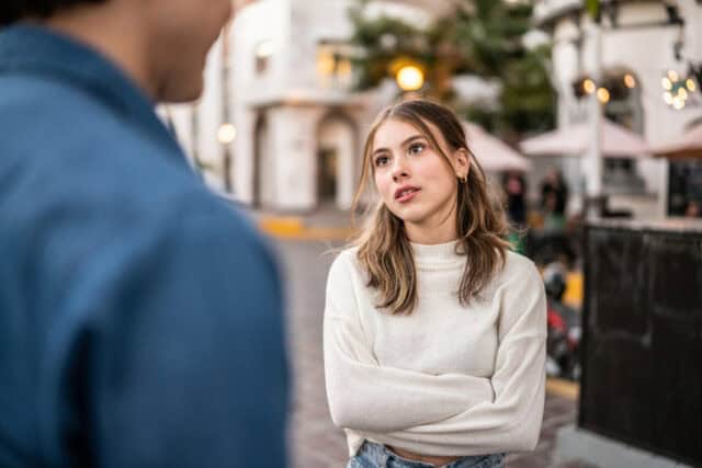 woman with crossed arms listening to man speak
