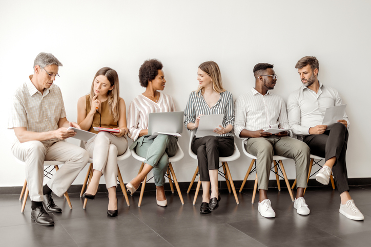 Diverse candidates sit on chairs and wait for an interview.