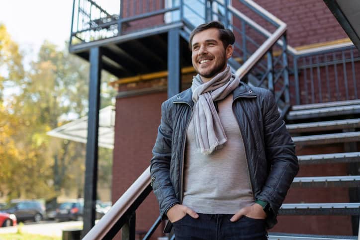 stylish adult man with a wide smile stands and looks at the street.