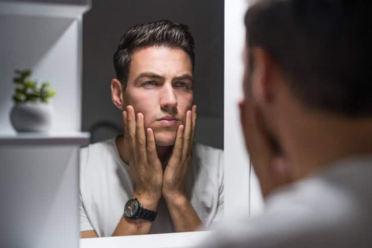 Man looking at his face in the mirror.