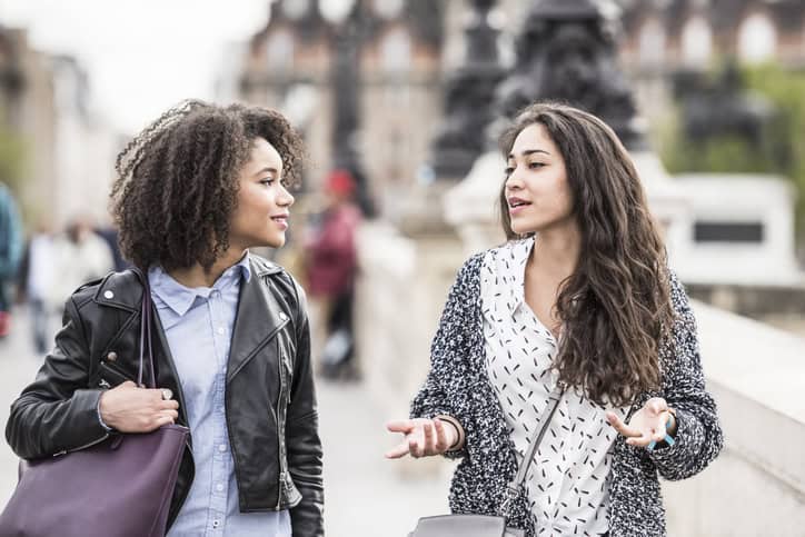Two young women walking in Paris street having conversation. Young woman gesturing with hands, female friend listening