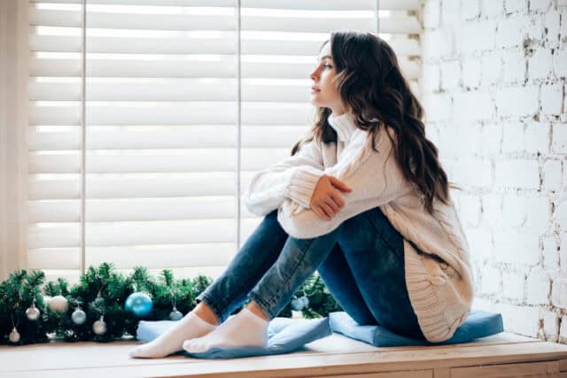 woman looking forlorn looking out window at christmas