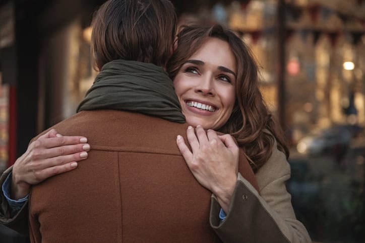 Portrait of happy young woman cuddling man with love. She is looking up dreamingly and laughing
