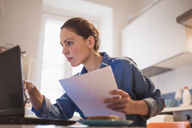 Woman using a laptop, browsing internet, holding documents