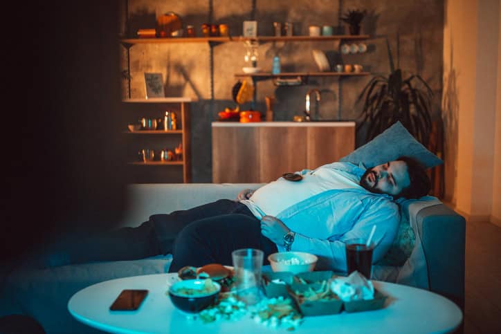 Man lying on the sofa and napping with junk food in front of him.