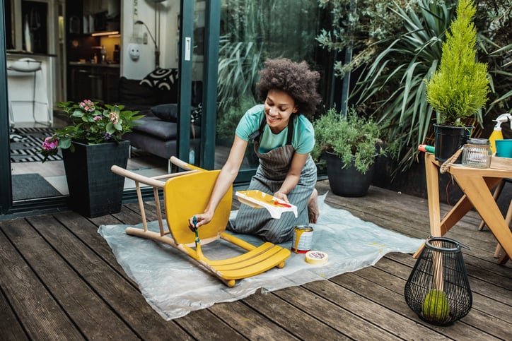 Female artist painting vintage chair in yellow.