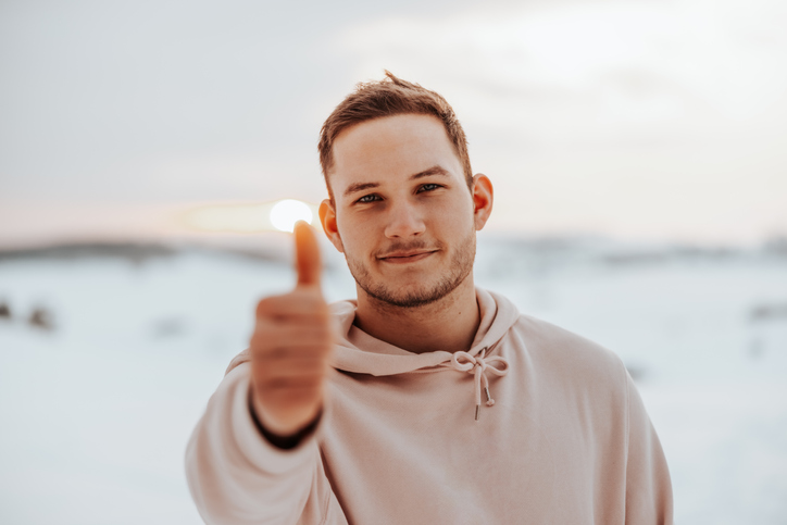 Smiling man standing in snow covered winter landscape showing a thumbs up.