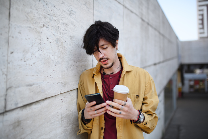 Young man texting outdoors with coffee.