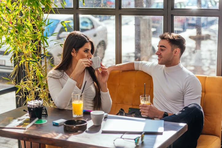 Two happy young people are laughing while sitting at a table in indoor café