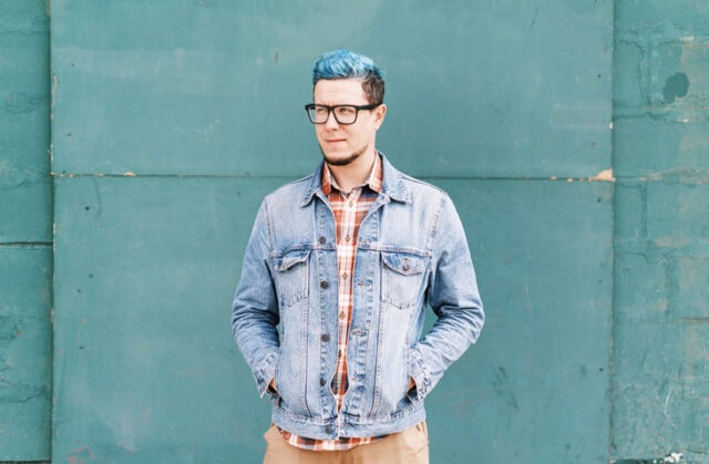 blue-haired man standing against blue wall