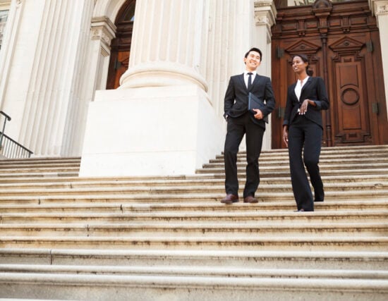 A well dressed man and woman smiling as they as they walk down steps of a courthouse building. Could be business or legal professionals.