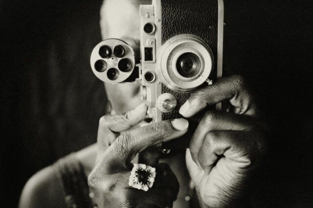 Portrait of a black female photographer. She is taking a picture with an old valuable analog camera.