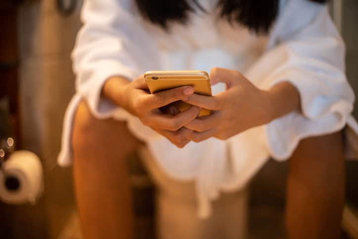 Woman holding a phone while using the toilet.