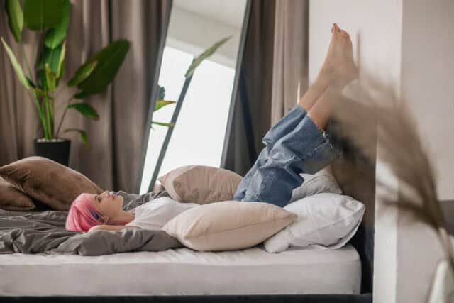 Tranquil relaxed pretty girl lying on the bed while raising her crossed legs against the wall