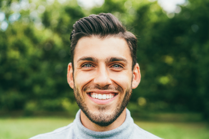 Smiling man with striking eyes in park.