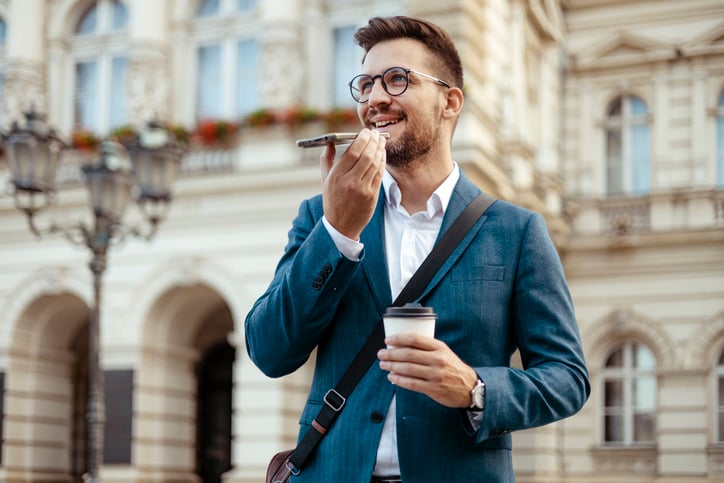 Urban Businessman Holding Smart Phone Communication Device Using Loudspeaker Answering to Incoming Call, Leave Voice Audio Message to Client Remotely. Virtual Assistant Usage Concept While Walking in City center