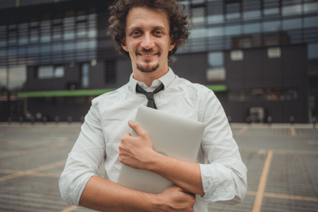 Portrait of happy young man in white shirt with tie looking at camera outdoors. A successful businessman in a city street.