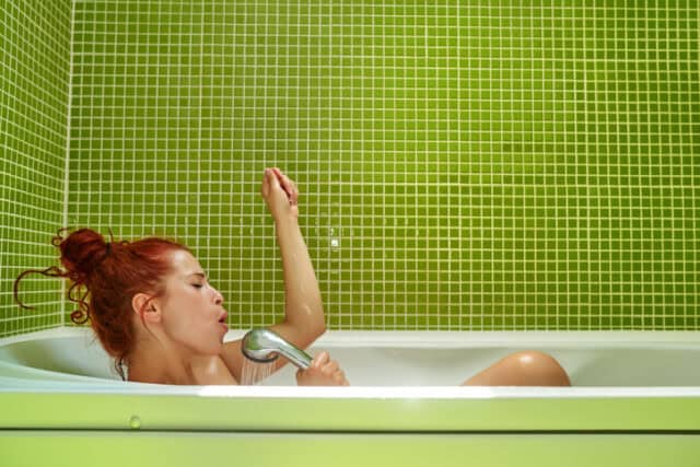 side view shot of woman in bathtub holding shower and singing, having fun and relaxing, lifestyle concept.