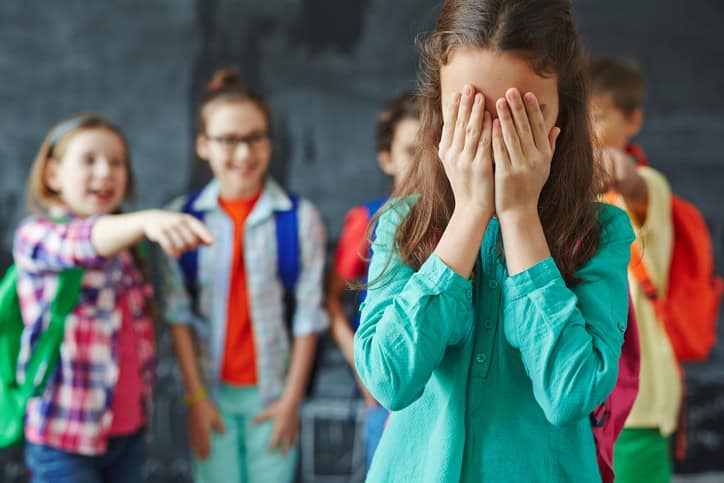Schoolgirl crying with classmates teasing her.