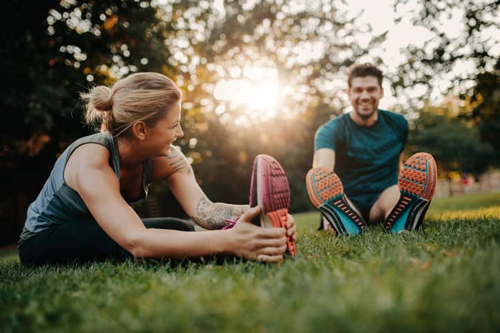 Man and woman stretching in park after run.