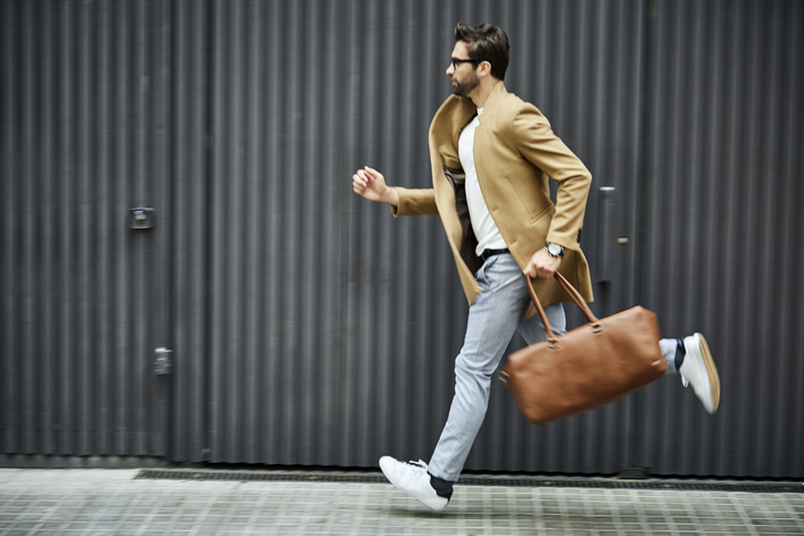Businessman with bag running on sidewalk in city.