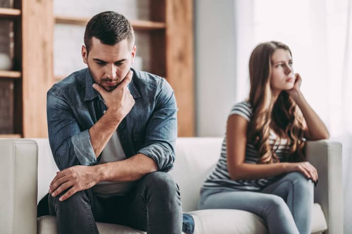 Upset couple at home. Handsome man and beautiful young woman are having quarrel. Sitting on sofa together. Family problems.